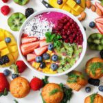 A variety of colored fruits and vegetables in and around the bowl